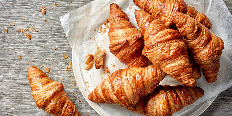 Varios croissants perfectamente cocinados y una pinta apetitosa en primer plano. 